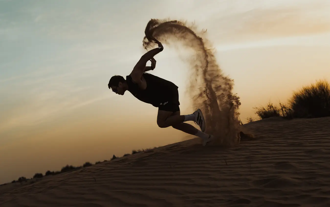 Athlete sprinting through a spray of sand on a dune at sunset