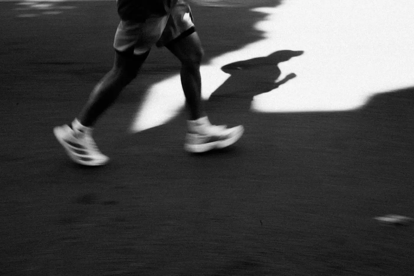 Runner's legs and long shadow on asphalt